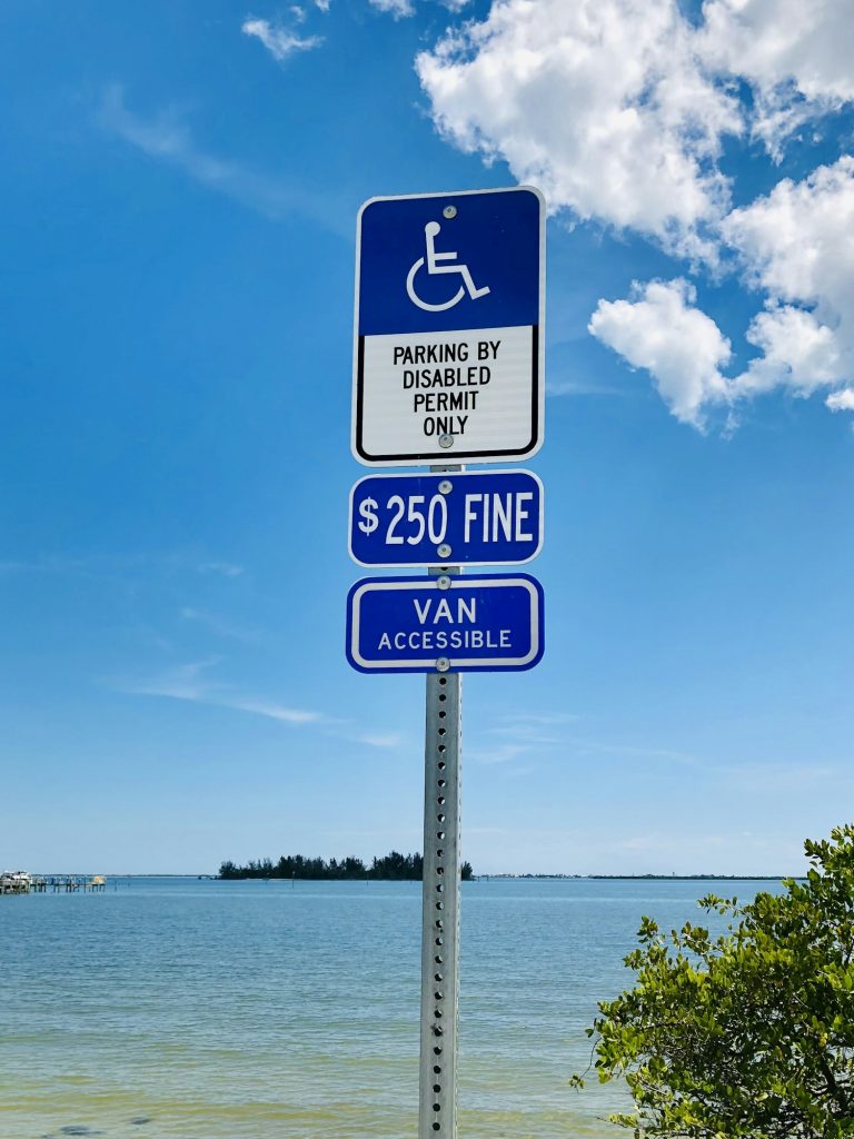A handicapped parking sign at the car park by the ocean.