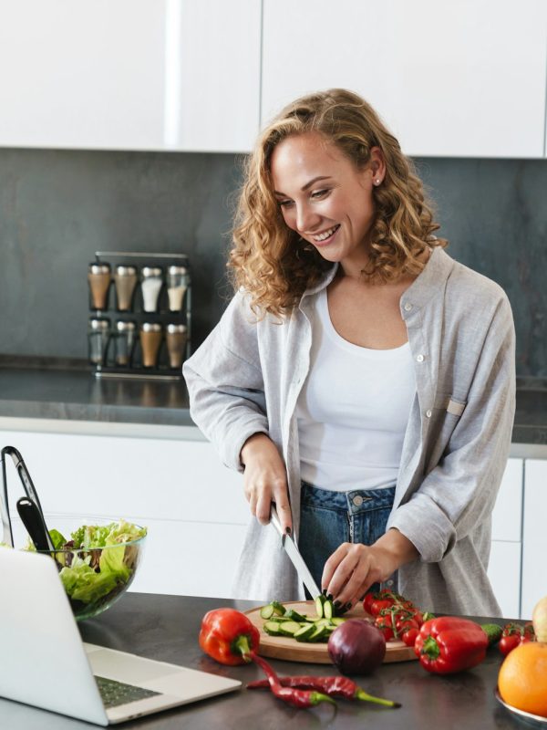 Happy young woman making a salad at the kitchen