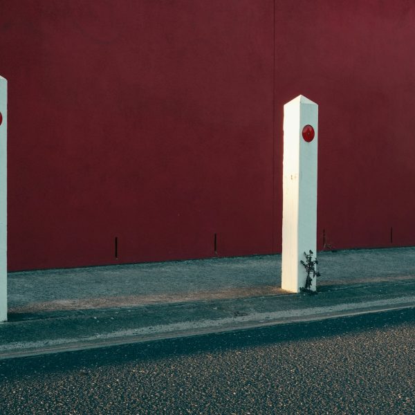 White parking poles alongside a road with a red wall in background
